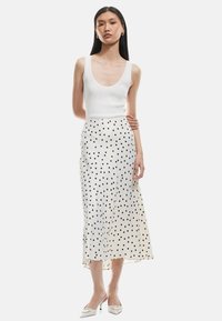 Vit ribbad linne i kombination med en flödande vit kjol med svarta prickar. Outfiten har en elegant siluett och knälång nederdel.