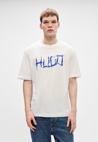 Tricou alb din bumbac cu un imprimeu grafic îndrăzneț de culoare albastră cu cuvântul "HUGO." Mâneci scurte și decolteu rotund. Croială lejeră.