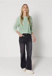 Ljusgrön långärmad skjorta matchad med svarta utsvängda jeans. Outfiten har en avslappnad passform och vita sneakers med gula accenter.