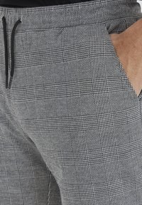 Gråternet joggers med en struktureret stof, snøre i taljen og sidelommer. Kendt for deres mønster og skræddersyede pasform.