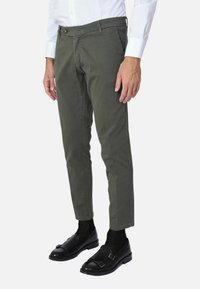 Pantaloni verde oliva con vestibilità slim, davanti piatto e passanti per cintura, realizzati in cotone. Presentano una chiusura anteriore con bottone e un design a gamba affusolata.