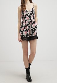 Svart blommig jumpsuit med rosa och gröna mönster, spagettiband, åtsittande byst, peplummidja och shorts med spetsdetaljer.