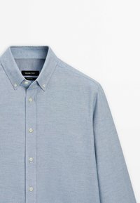 Chemise bleu clair à boutons, manches longues et col, avec des boutons couleur crème et une étiquette Massimo Dutti à l'intérieur du col.