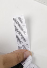 Bijela oznaka za njegu tkanine koju drži ruka, s ispisanim tekstom na više jezika o sastavu tkanine i uputama za pranje.