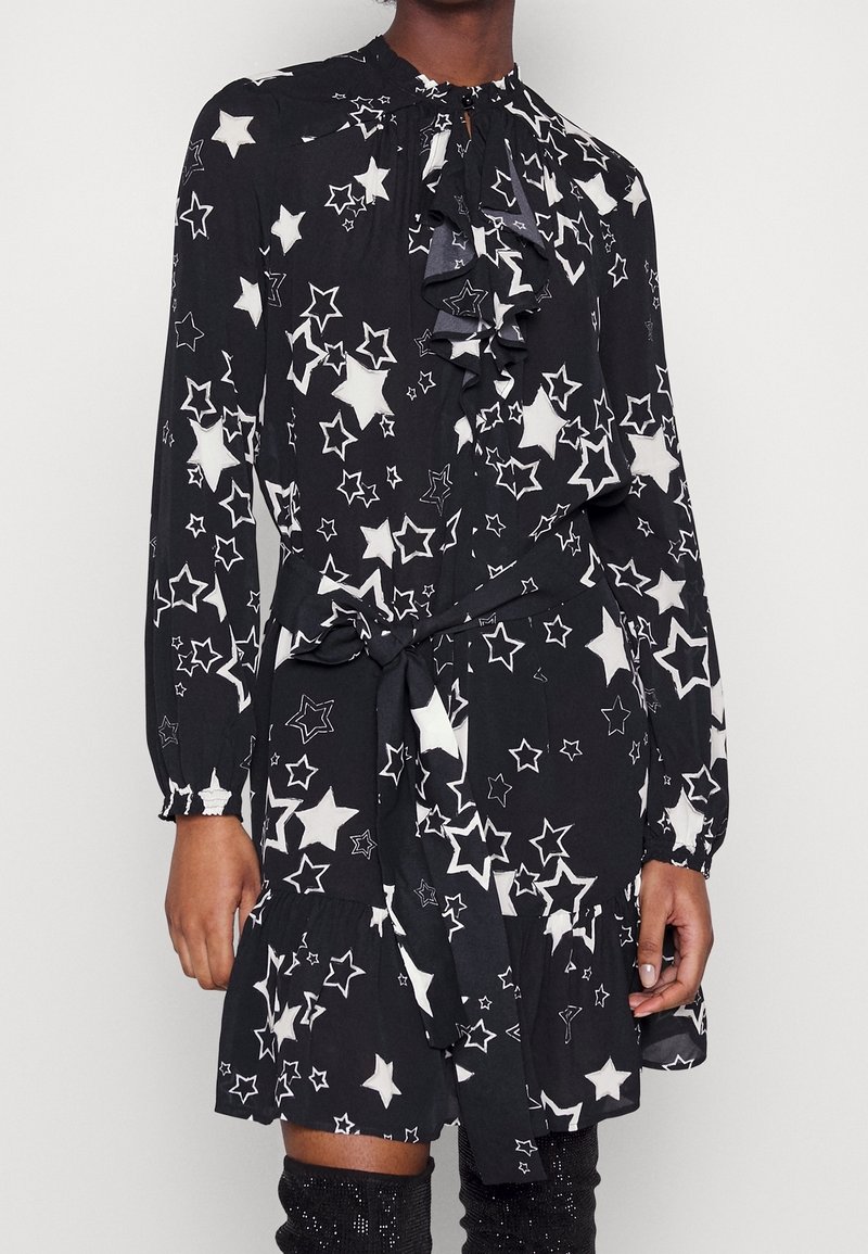 Musta mekko, jossa on valkoinen tähtikuosi, rypytetty kaula-aukko, pitkät hihat nappikiinnityksellä ja vyönauha vyötäröllä, teksturoitu kangas.