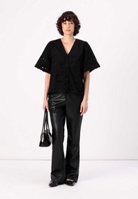 Black cotton top with short, flared sleeves and eyelet embroidery, paired with black faux leather flared pants and black flats, holding a small bag.