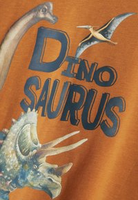 Tessuto arancione con illustrazioni colorate di teste di dinosauro. Testo "DINOSAURUS" ben in evidenza in blu scuro, con varie texture visibili.