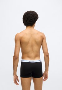 Mustad bokserpüksid helesinise vööga, millel on "TOMMY HILFIGER" logo, valmistatud pehmest ja elastse materjaliga. Vaade tagant.