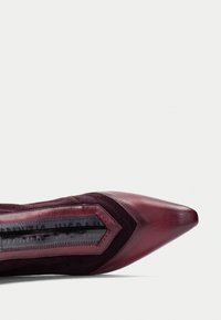 Špičaté lodičky z hluboké burgundy kůže se semišovými akcenty. Disponují texturovanou inlay a kontrastním prošíváním podél stran.