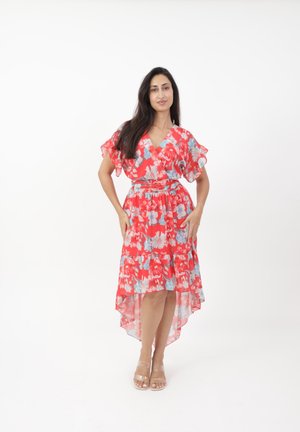 Rode bloemenjurk met korte flapmouwen, een wikkelontwerp en een hoge-lage zoom. Bevat blauwe bloemen en een getailleerde taille. Doorzichtige sandalen met hakken.