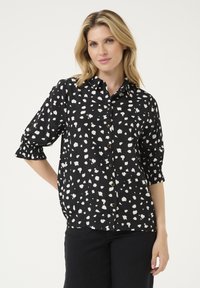 Schwarze Hemdbluse mit weißem Spritzer-Muster, Dreiviertelärmel und Raffung an den Manschetten. Glatte Stoffstruktur.