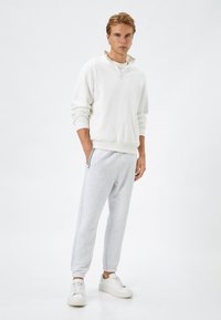 Jasnoszara bluza z wysokim kołnierzem i zamkiem, zestawiona z jasnoszarymi joggerami o tapered i białymi sneakersami. Miękki, odporny na pot materiał.