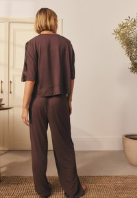 Set de pijama maro, care include un top lejer cu mâneci scurte și pantaloni cu picior larg asortați, realizat dintr-un material moale și ușor.