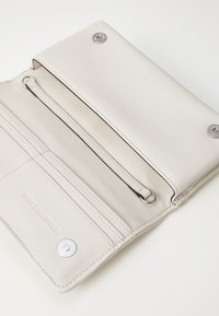 Portafoglio bianco in pelle dal design semplice, con tasca con zip, scomparti per carte e chiusura a scatto argentata. Texture liscia, senza motivi visibili.