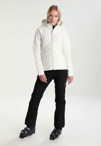 White insulated ski jacket with a zip front and hood; worn with black ski pants and boots; designed for cold weather sports.