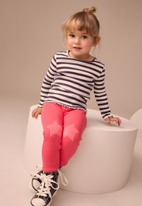 Striped long-sleeve shirt in navy and white, paired with pink leggings featuring soft star appliqués. Black sneakers with white laces.