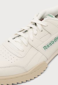 Λευκό δερμάτινο αθλητικό παπούτσι Reebok με λευκά κορδόνια, διάτρητη περιοχή στα δάχτυλα και πράσινο λογότυπο Reebok στο πλάι και στη γλώσσα.