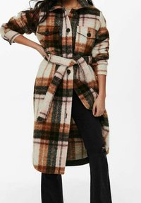 Manteau en polaire à carreaux dans les tons marron, crème et vert. Il présente une fermeture à boutons sur le devant, deux poches poitrine et une ceinture à la taille. Manches longues.