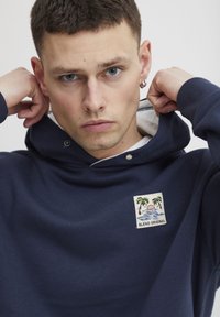 Navy blue hoodie made of soft cotton, featuring a front patch with palm trees and water, and a drawstring adjustable hood.