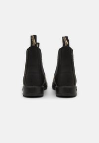 Botines de cuero negro con un acabado suave, paneles laterales elásticos y tiradores en la parte trasera, con un tacón bajo y grueso.