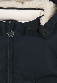Czarna kurtka z zewnętrznego materiału z białym polarowym wykończeniem, z zamkiem błyskawicznym, zatrzaskami i suwakiem w kształcie niedźwiedzia.