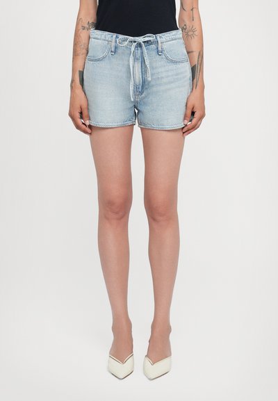 Shorts en denim bleu clair avec une taille à cordon, des poches avant, une coupe classique et un ourlet effiloché. Portés avec des talons blancs en pointue.