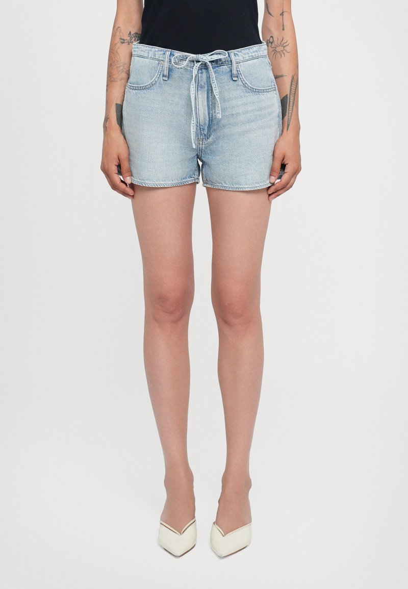 Shorts en denim bleu clair avec une taille à cordon, des poches avant, une coupe classique et un ourlet effiloché. Portés avec des talons blancs en pointue.