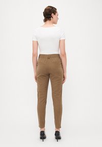 Hvid kortærmet top og brune fløjelsbukser med en smal ben. Bukserne har høj talje, elastisk taljebånd og baglommer.