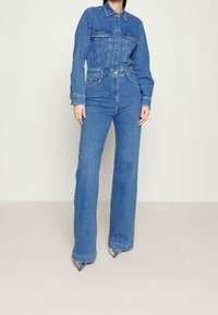Denim jumpsuit i ljusblått, med knäppning fram, två bröstfickor, långa ärmar och utsvängda ben. Texturerad tyg med en klassisk design.