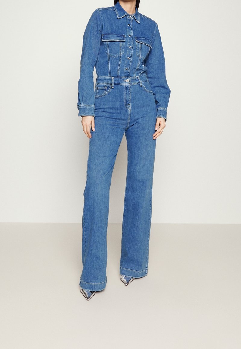 Denim jumpsuit i ljusblått, med knäppning fram, två bröstfickor, långa ärmar och utsvängda ben. Texturerad tyg med en klassisk design.