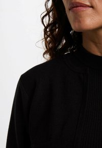 Suéter negro de punto con cuello alto, textura acanalada y sutiles detalles de costura a lo largo de los hombros y el escote.