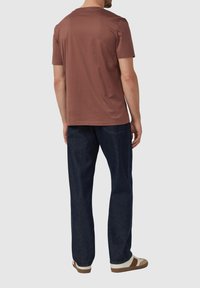 Hnedé tričko s krátkym rukávom a okrúhlym výstrihom, skombinované s tmavomodrými džínsami a béžovo-hnedými topánkami, zobrazené zozadu.