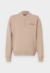 Beige svetr s podšívkou, žebrovanými manžetami a lemem, s vyšitou logem "Tommy Hilfiger" na hrudi. Měkký materiál, uvolněný střih.