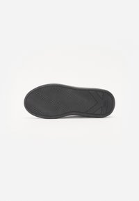 Black rubber shoe sole with a textured wavy pattern, featuring an angular design on the heel side and smooth edges.