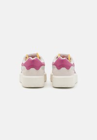 Zapatillas con un acento en el talón de cuero rosa, ante gris y parte superior de malla blanca. Suela gruesa de goma blanca, patrón de rodadura negra y forro interior amarillo.