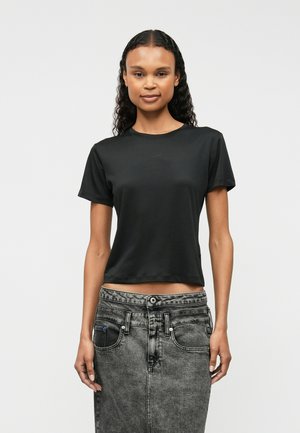 Black short-sleeve cropped t-shirt in a smooth fabric. Features a round neckline and relaxed fit, paired with high-waisted gray denim.