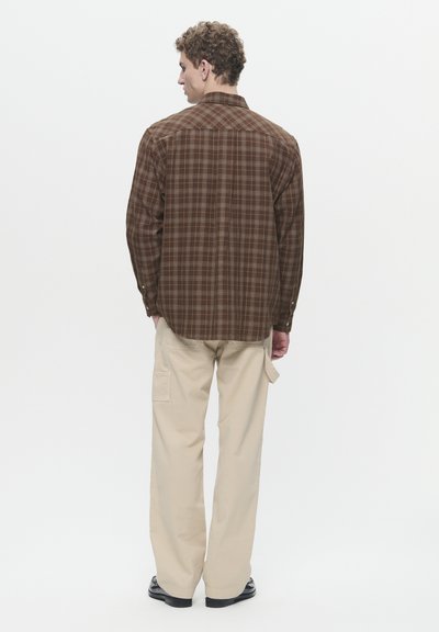 Chemise à carreaux marron à manches longues et poignets boutonnés, associée à un pantalon cargo beige. Texture de tissu lisse, design de col simple et motifs subtils.