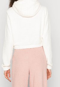 Korte witte fleece hoodie met een gestructureerd oppervlak en een capuchon, gecombineerd met roze, zachte, fuzzy broek.
