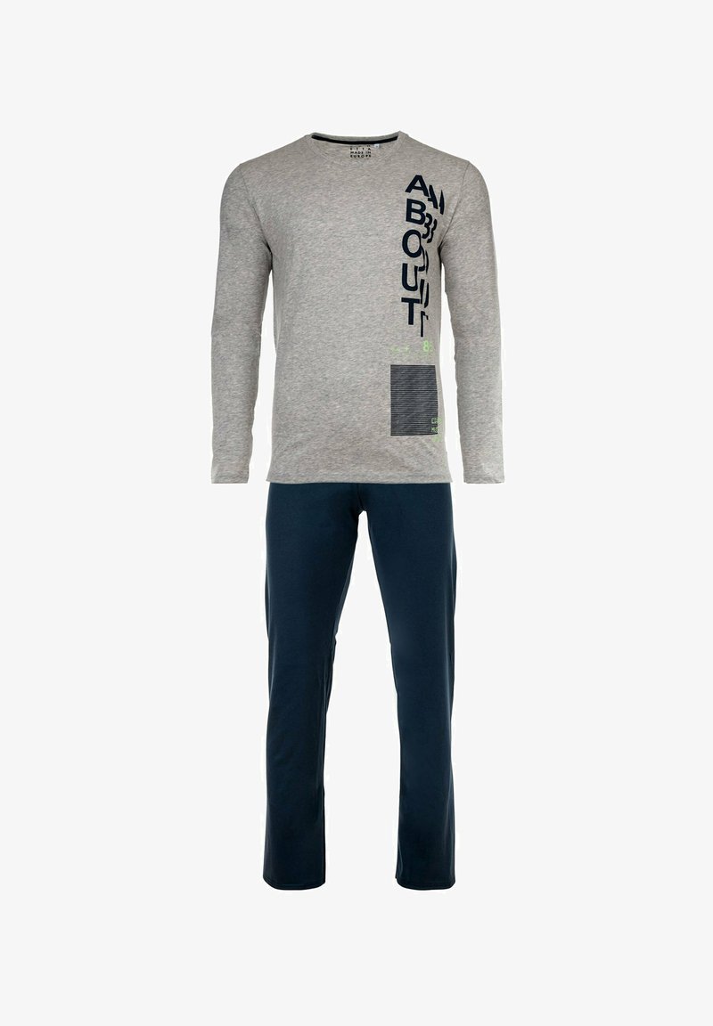 Grijze langemouwen T-shirt met tekst en designelementen; gecombineerd met marineblauwe broek. De stof lijkt zacht en casual.