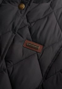 Zwarte gecapitonneerde jas met een bruine leren Superdry® logo patch en messing drukknoopdetails. Soepele textuur met een diamantpatroon stiksels.