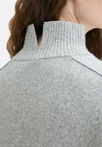 Pulover tricotat de culoare gri deschis, cu un guler înalt cu model de nervuri, având un design despicat în spate, ce pune în evidență un material texturat și modele subtile.