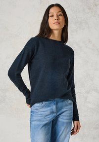 Dunkelblauer Strickpullover mit langen Ärmeln und rundem Halsausschnitt, getragen über hellblauen Jeans, mit weichem Material und bequemer Passform.