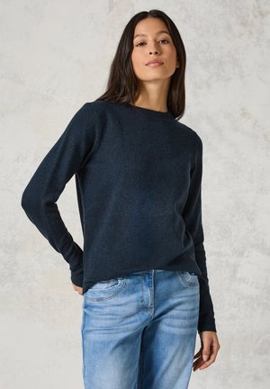 Marinblå stickad tröja med långa ärmar och rund halsringning, buren över ljusblå jeans, med en mjuk textur och avslappnad passform.