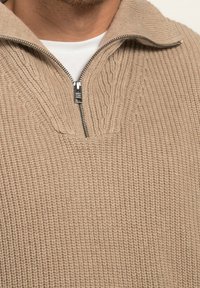 Pullover beige lavorato a maglia con colletto a zip a quarti e design a costine testurizzate. Il tessuto appare morbido e ha una vestibilità rilassata.