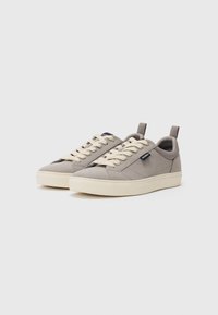 Grey canvas sneakers with cream laces and sole, featuring a pull tab at the back and a logo patch on the side. Smooth texture, simple design.