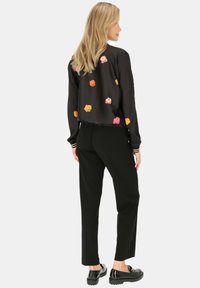 Czarna krótka bluzka z kolorowym haftem kwiatowym, zestawiona z czarnymi spodniami i błyszczącymi czarnymi butami na płaskiej podeszwie.
