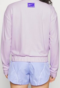 Sudadera lila con cinturilla ajustada y logo de Nike TEAM en púrpura. Combinada con pantalones cortos azul claro que cuentan con detalles de ribete en los laterales.