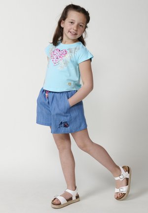 T-shirt bleu clair à manches courtes avec un motif de cœur et un design d'ailes, associé à un short bleu avec des poches latérales et un accent brodé.