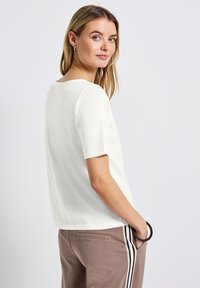 T-shirt bianco a maniche corte con scollo rotondo e vestibilità comoda, abbinato a pantaloni marroni con strisce laterali. Tessuto morbido.