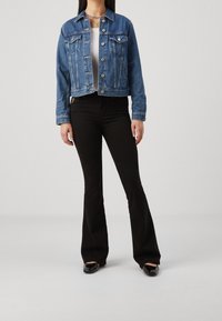 Keskitummansininen farkkutakki, jossa napitettava etuosa ja rintataskut, yhdistetty korkeavyötäröisiin mustiin liehuviin farkkuihin. Yksinkertainen valkoinen t-paita alla.